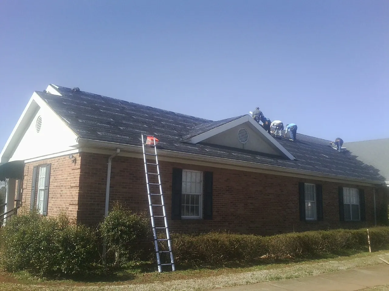 Crew tearing shingles off a brick ranch roof with a ladder set — Emergency Roof Repair work by our crew in Ainsworth