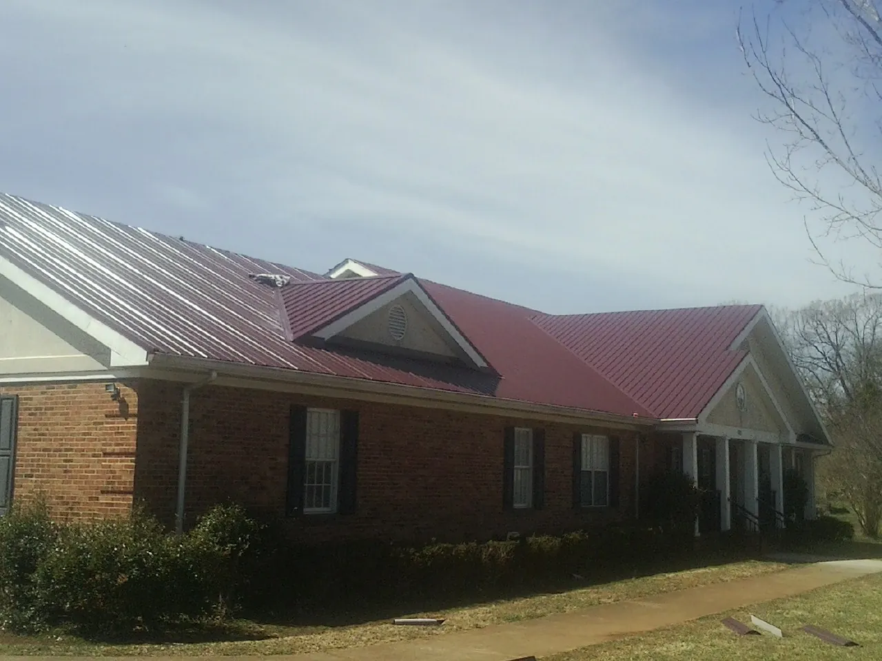 Red metal roof with gabled entries on a long brick building, from a Hail Damage Roof Repair job in Ainsworth