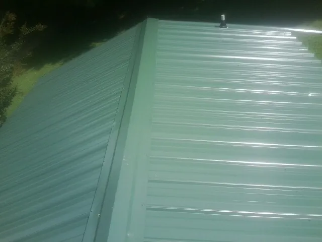 New green metal panels meeting at the ridge of a roof — Flat Roof Repair work by our crew in Ainsworth