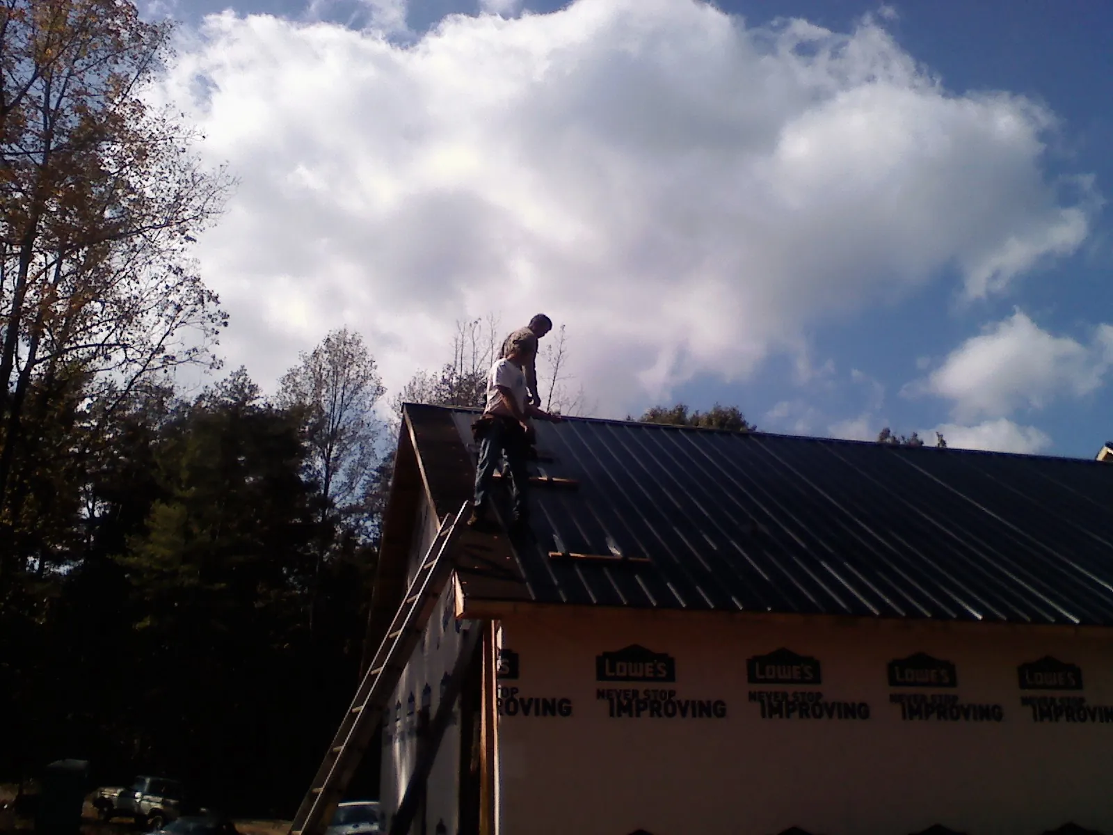 Roofer fastening dark metal panels high against a cloudy sky, from a Roof Inspection job in Ainsworth