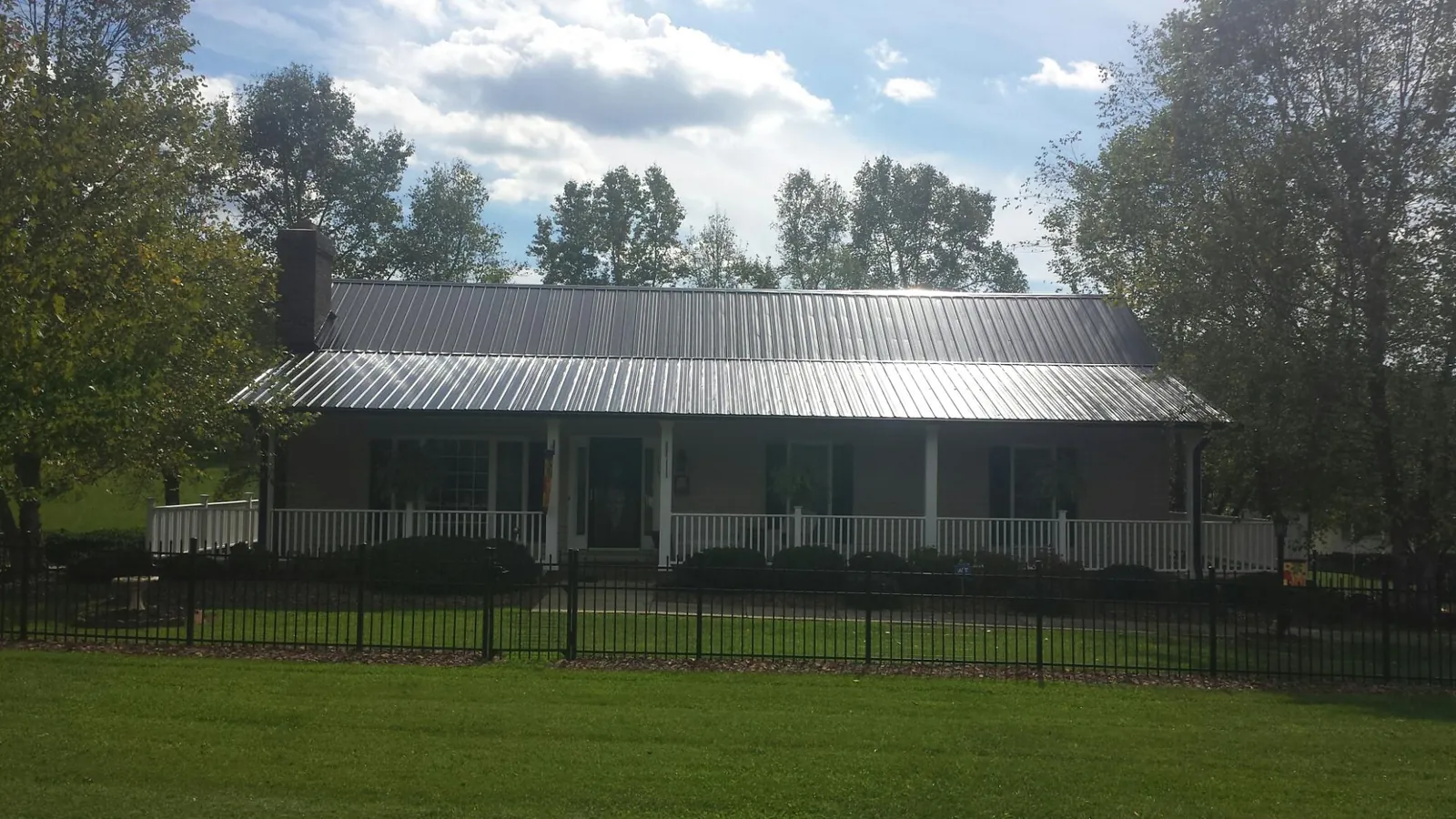 Gray metal roof on a brick ranch with a full width front porch — Gutter Guard Installation work by our crew in Ainsworth