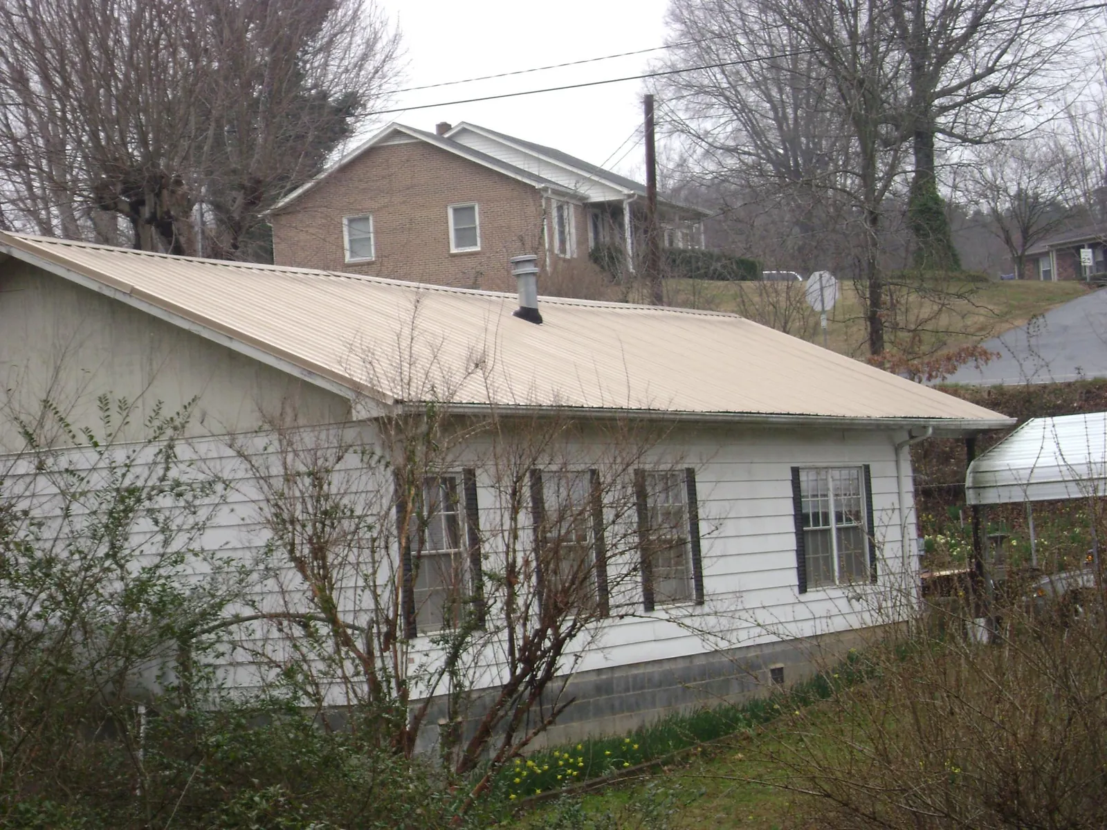 Tan metal roof on a white sided house set into a hillside — Commercial Roofing by Roofing Brothers in Ainsworth