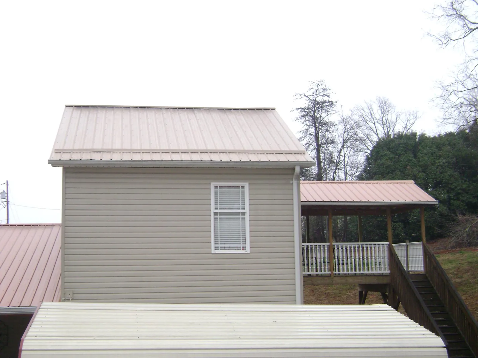 Tan metal roofs on a two story addition and attached porch, from a Roof Replacement job in Ainsworth
