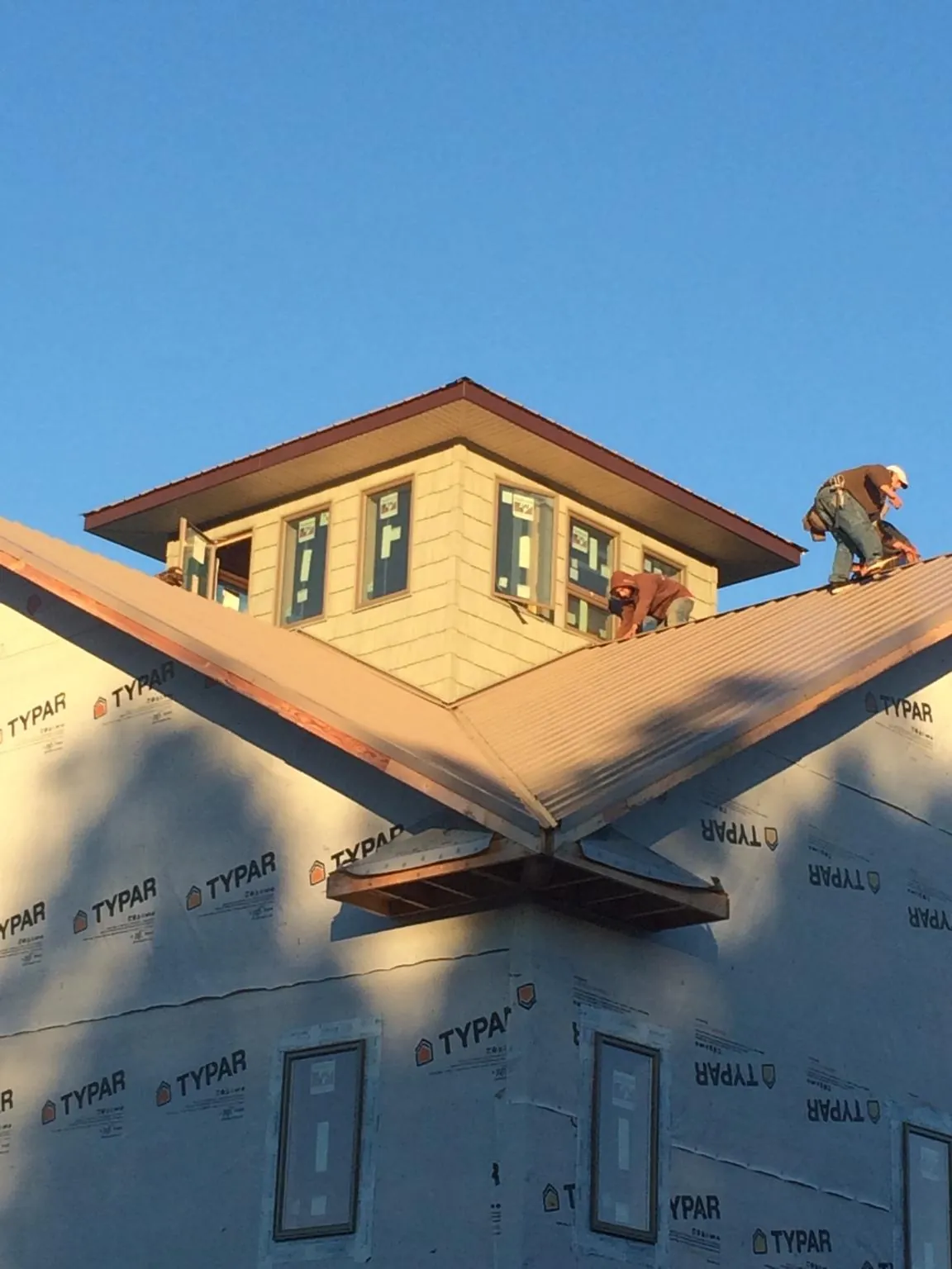 Roofers working around a rooftop cupola on a new metal roof at sunset — Roof Waterproofing in Ainsworth by Roofing Brothers